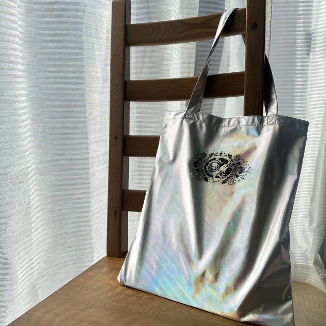 <p>折りたたんでコンパクトに持ち運べるトートバッグ。中面にある袋に折りたたんで収納可能。出先で荷物が増えても、さっと広げて活躍。A４サイズの本もすっぽり入ります。オーロラ&times;シルバーカラー。ハートのカラビナ付で、バッグにぶら下げて持ち運べます。<br><br>[サイズ] 幅33cm&times;高さ37cm<br>　　　　（収納時）：幅10.5cm&times;高さ10cm<br>[素材]ポリエステル<br>※数量限定のため無くなる可能性がございますので、ご了承ください。</p>
